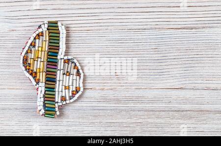 needlecraft background - top view of handcrafted brooch from various glass bugles and beads on gray wooden board with copyspace Stock Photo