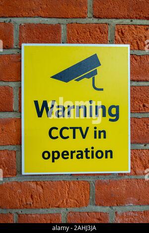 Yellow and black Warning CCTV in operation sign on a red brick wall Stock Photo