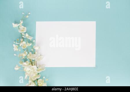 Mothers day or wedding floral card with paper note and white flowers over a blue background shot from above. Flat lay. Stock Photo