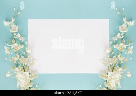 Mothers day or wedding floral card with paper note and white flowers over a blue background shot from above. Flat lay. Stock Photo
