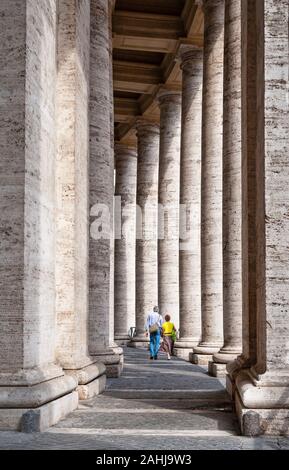 Older middle aged tourist couple walking among tall columns of  Bernini's colonnade in St. Peter's Square, Vatican City, Rome, Italy Stock Photo