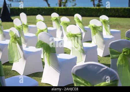 wedding chairs that cover with white cloth and decorate with soft green cloth for guest in ceremony, have beach on background Stock Photo