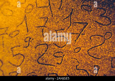 Hand drawn different numbers on shiny sand, a numerical background on gold. Stock Photo