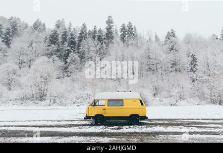 Carpathians, Ukraine - December 2019: yellow camper van with winter snowy forest on background Stock Photo