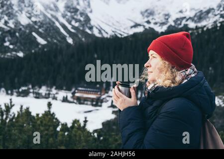 Woman having a hot drink from thermos cup overlooking snowcapped High Tatra mountains peaks Stock Photo