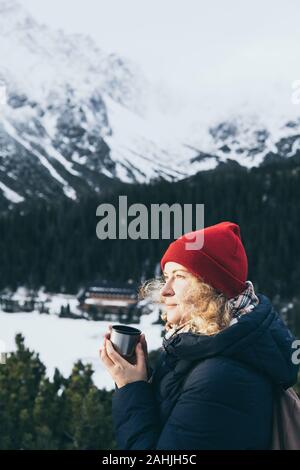 Woman having a hot drink from thermos cup overlooking snowcapped High Tatra mountains peaks Stock Photo