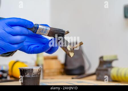 Hand in blue rubber gloves paints metal parts with black paint brush. Stock Photo