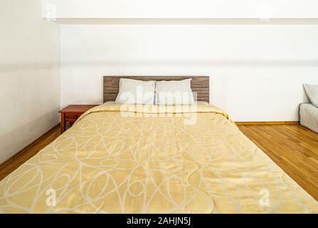 Front view of king-size bed covered with yellow blanket in spacious bedroom. White walls. Stock Photo