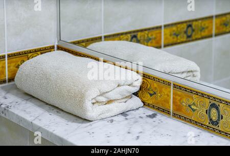A white folded towel on a marble shelf next to the mirror. Close-up. Stock Photo