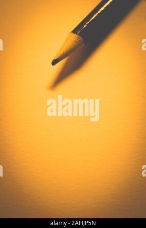 Pencil on clean paper, orange warm tone, copy space. Stock Photo