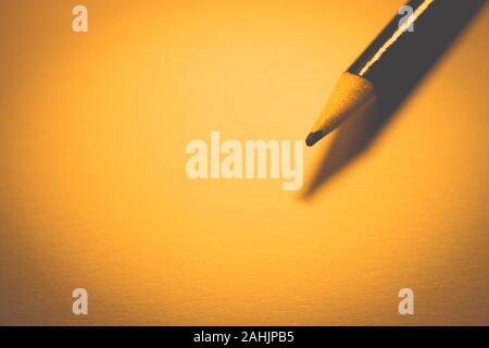 Pencil on clean orange paper, warm tone, copy space. Stock Photo