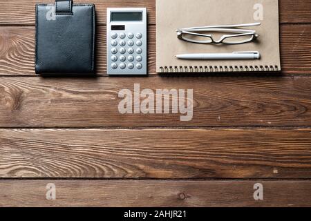 Still life of accountant workspace with office accessories. Flat lay old hardwood desk with black leather wallet, calculator and notepad. Accounting a Stock Photo