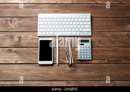 Top view of accountant workspace with office accessories. Flat lay wooden desk with computer keyboard, calculator and smartphone. Accounting and banki