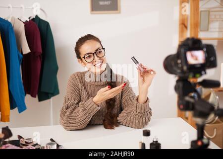 Portrait of smiling young woman showing make up products to camera while filming video for beauty and lifestyle channel, copy space Stock Photo