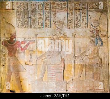 Luxor in Egypt, Karnak site, temple of Opet. The king, wearing a white crown, bracelets and a collar, offers small vases to Amonet and Isis the Great. Stock Photo
