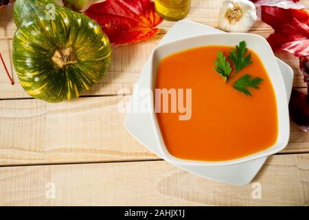 igh Angle view Of pumpkin Ssoup served In bowl with autumn leaves On table. Stock Photo