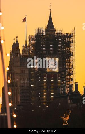Westminster, London, 30th Dec 2019. The new blue and gold-leaf coloured clock face of the Elizabeth Tower is visible on the Houses of Parliament,  silhouetted at sunset. A beautifully sunny winter day in London concludes with a soft pastel sunset in Westminster. Credit: Imageplotter/Alamy Live News Stock Photo