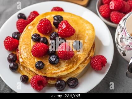 Sweet homemade pancakes with raspberries on white plate on grey table.