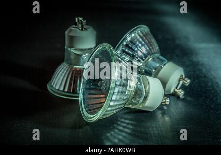 Three halogen light bulbs two sitting on an angle with light reflecting on the bulbs indoors close up on a black background Stock Photo
