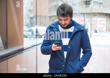 Handsome young man, standing outside the office building, using mobile phone while having a break at work . Stock Photo