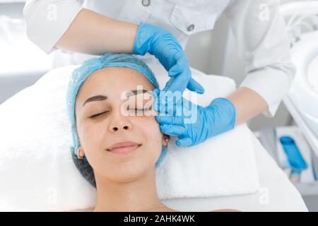 Beautician makes a young beautiful girl a relaxing and wellness facial massage. Facial care and rejuvenation Stock Photo