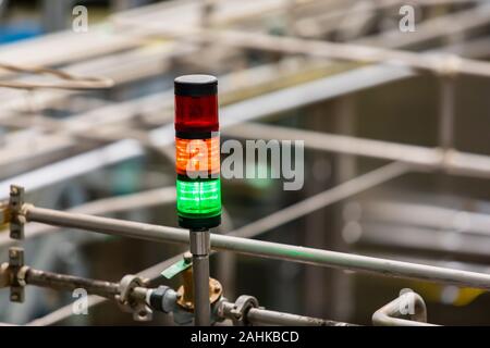 Selective focus three colors signal lamp, red, orange, with the green light on, metallic pipes in the conveyor systems background, copy space Stock Photo