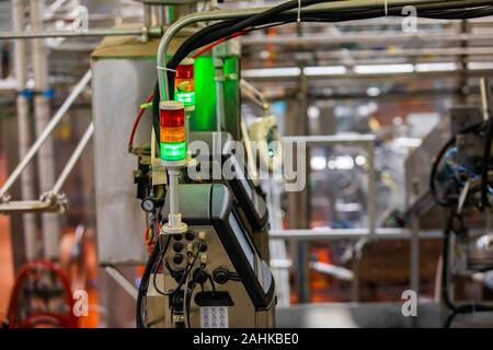 Selective focus three colors signal lamp and monitoring system, with metallic pipes and conveyor belt systems in the background, for industrial beer brewing Stock Photo