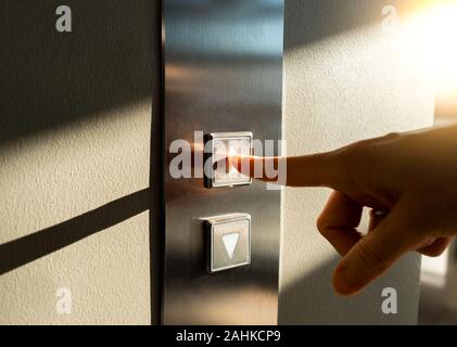 a woman's finger presses the Elevator button in the sunlight Stock Photo