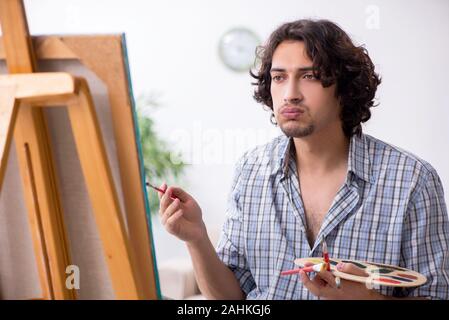 The young handsome man enjoying painting at home Stock Photo