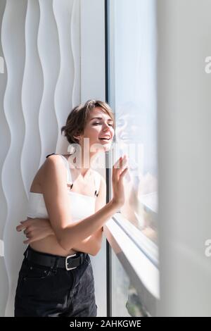 Happy woman thinking and looking at side beside a window at home Stock Photo