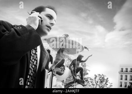 Side view of a man talking on his cell phone with a fountain in the background. Stock Photo