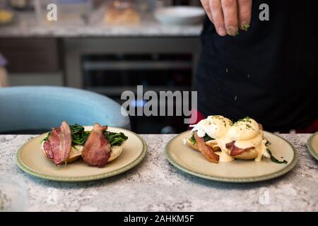 Eggs benedict with crisp bacon and spinach being topped with hollandaise sauce for morning brunch. Stock Photo