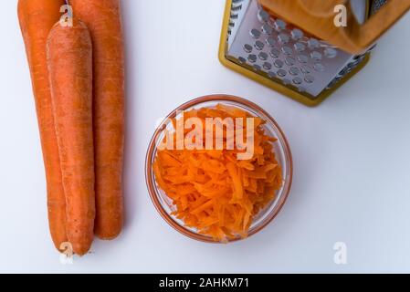 Fresh Grated carrot in a bowl and layout of carrots and grater isolated on white background Stock Photo