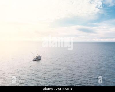 A small old fishing trawler on the open ocean with clouds on the horizon. Stock Photo