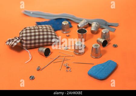 Image of sewing needles, thimbles of different sizes, a chalk marking the fabric (tailor) on an orange background Stock Photo
