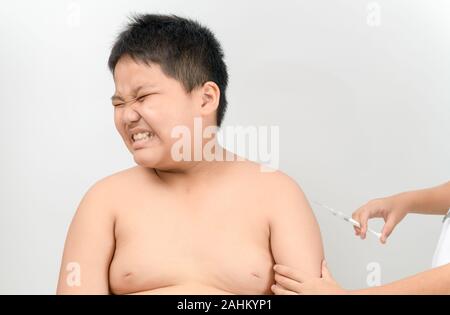 Fat boy afraid of syringe turning his head away squeezing eyes in fear. Medical assistant giving an intramuscular injection of a vaccine to his arm. V Stock Photo