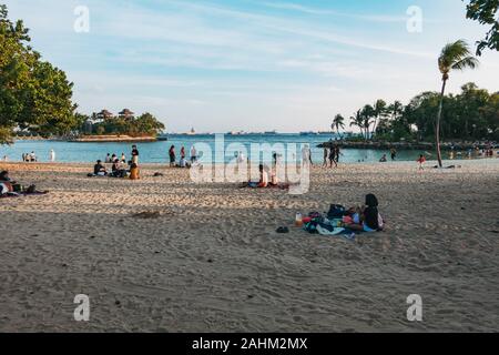 Beachgoers relax in the evening at man-made Palawan Beach, Sentosa Island, Singapore Stock Photo
