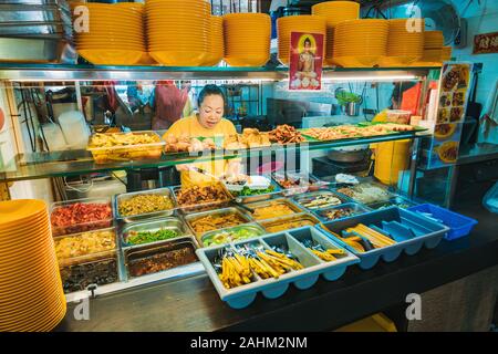 A woman scoops food onto a plate at a Buddhist vegetarian food stall in the Waterloo Food Centre, Singapore. Stock Photo