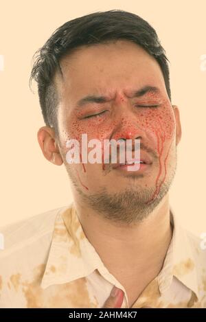 Face of young crazy Asian man looking sad with eyes closed and blood on face Stock Photo