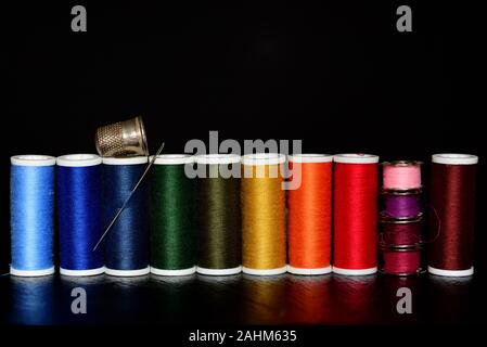 Still life of different rolls of sewing thread in rainbow colors, with sewing needle, thimble and spools of thread for the sewing machine against a da Stock Photo
