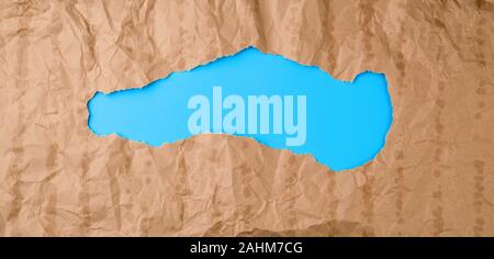 crumpled paper texture from a brown sheet of paper with greasy spots and a large hole. abstract banner for the designer, blue backdrop. Stock Photo
