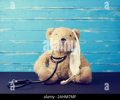 teddy bear is sitting in a white medical mask, black stethoscope is hanging on his neck, concept for treating children Stock Photo