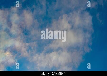 Thin, fluffy clouds are dusting an otherwise blue sky, and in the light of early sun have a slight purple hue. Stock Photo