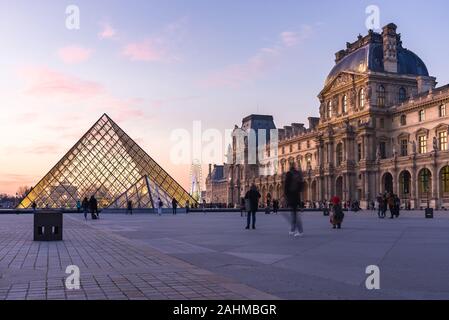 Pyramide du Louvre and Angelina Paris Musée du Louvre at sunset with people walking outside, Paris, France Stock Photo
