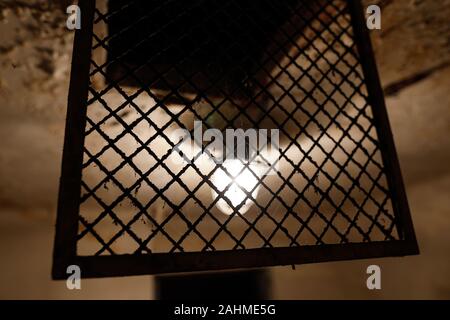 Grungy image with the light bulb and a metallic net on a worn out ceiling in an old prison cell. Stock Photo