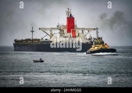 Coal Bulk Carrier with Tugboats Leaving Port of Newcastle with small fishing boat in foreground, Australia Stock Photo