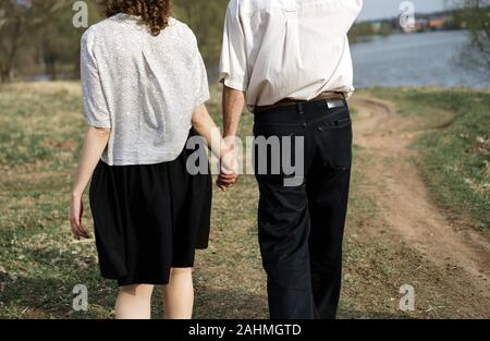 Loving couple elderly man and a young girl walking together hands on nature Stock Photo