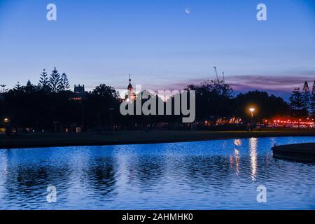 Newcastle Evening and Reflection in Pond at Foreshore Park with Trees, Customs House, Christ Church Cathedral and Moon in Background Stock Photo