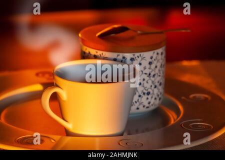Hot coffe in the afternoon sun on wooden table on metal plate with sugar and spoon on jar Stock Photo