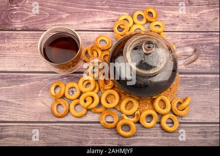 Bagels, a glass of tea and a glass teapot of tea on a wooden background. The view from the top Stock Photo
